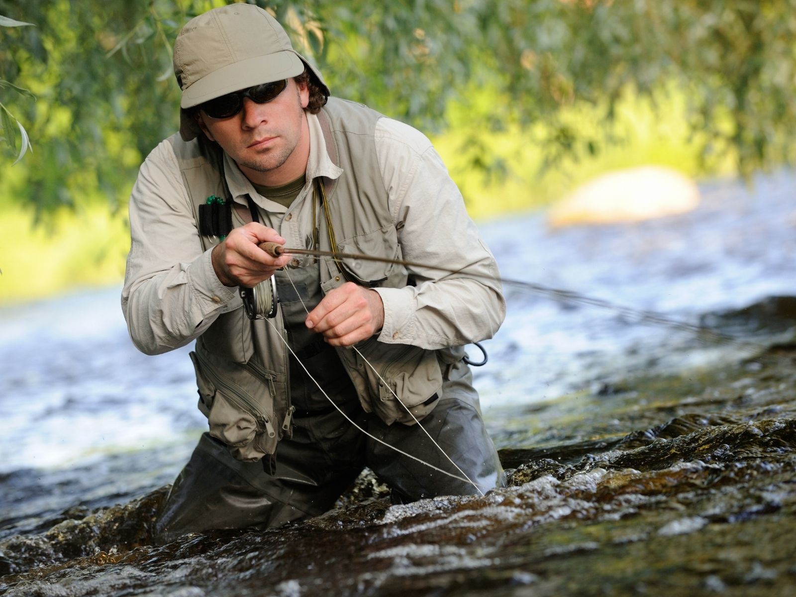Fishing Hat Wearing Fly Fisherman casting a fly while wading in a stream