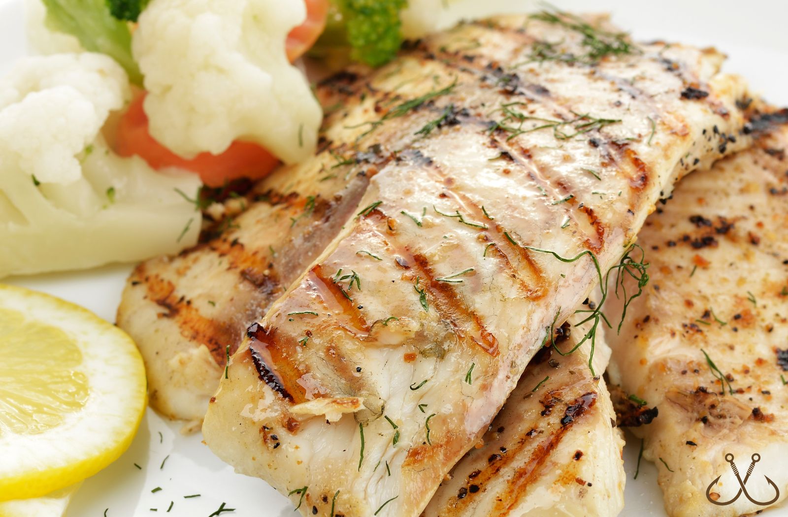 Grilled redfish on a plate with mixed veggies and lemon slices
